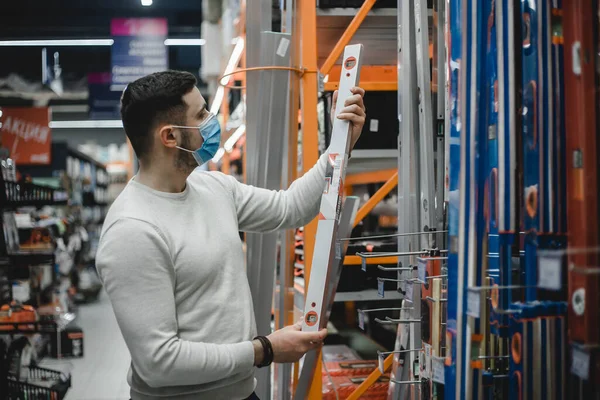 Young carpenter wearing disposable medical mask holding a builders level in a hardware store. Royalty Free Stock Images