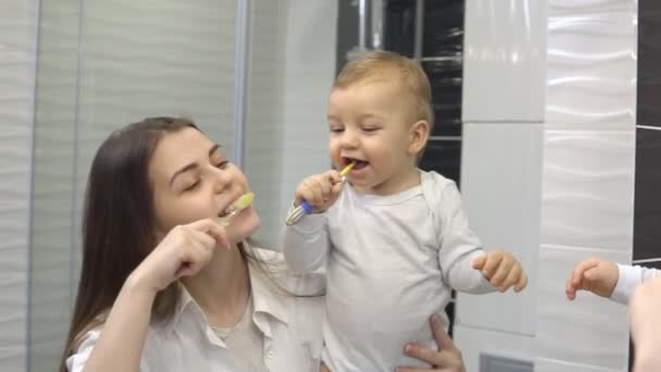 Χαμογελαστή μητέρα και ο γιος αγοράκι βουρτσίζουν τα δόντια τους μαζί με οδοντόβουρτσα. Η μαμά μαθαίνει στο χαριτωμένο παιδί πώς να βουρτσίζει τα δόντια — Αρχείο Βίντεο