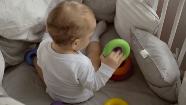 Niedliches Baby spielt mit bunten Regenbogen-Spielzeug-Pyramide sitzt im Bett. — Stockvideo