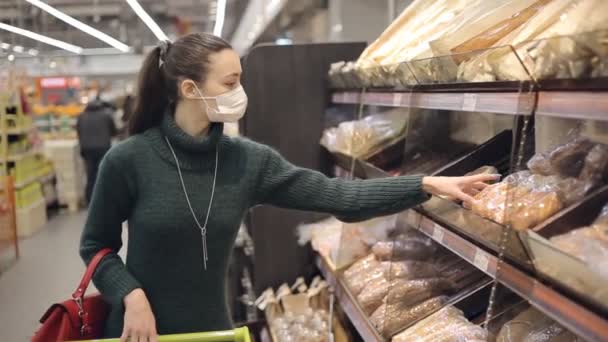 Donna che indossa una maschera medica usa e getta scegliere il pane durante lo shopping al supermercato panetteria. Protezione e prevenzione delle misure durante il periodo epidemico. — Video Stock