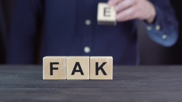 Un homme en chemise compose le mot FAKE à partir de cubes en bois — Video