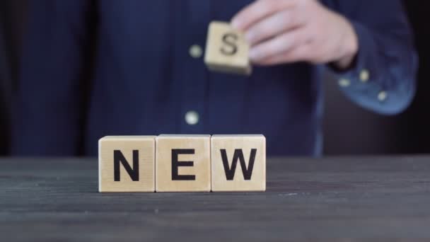 Gömlekli bir adam ahşap küplerden "yeni haber" kelimesini yazıyor. — Stok video