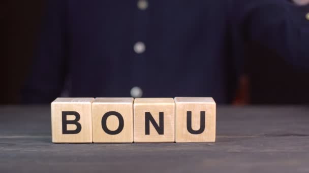 Muž v košili skládá slovo BONUS z dřevěných kostek, zblízka — Stock video