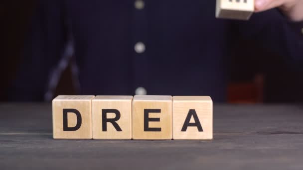 Egy férfi ingben alkotja a szó DREAM fából kockák, közelről — Stock videók
