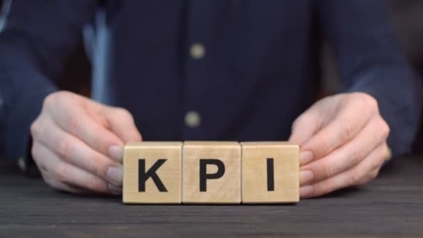 Un hombre con una camisa mostrando la palabra KPI de cubos de madera, de cerca — Vídeos de Stock