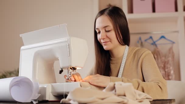 Mujer joven haciendo ropa usando máquina de coser. Sentada en su lugar de trabajo en casa — Vídeos de Stock
