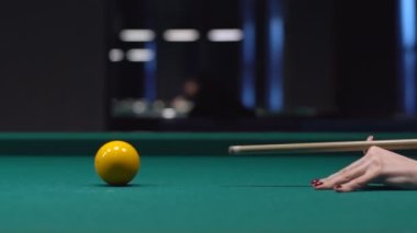 Bir kadın eli bilardo masasında bilardo topuna vuruyor, sarı topa nişan alıyor.
