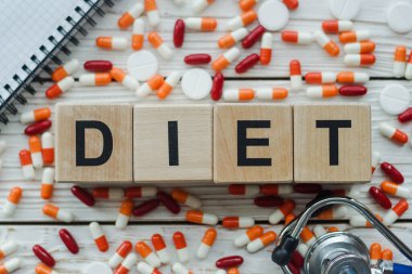 Diyet kelimesi beyaz arka planda haplar ve steteskopla bulunan tahta küplerden oluşur..