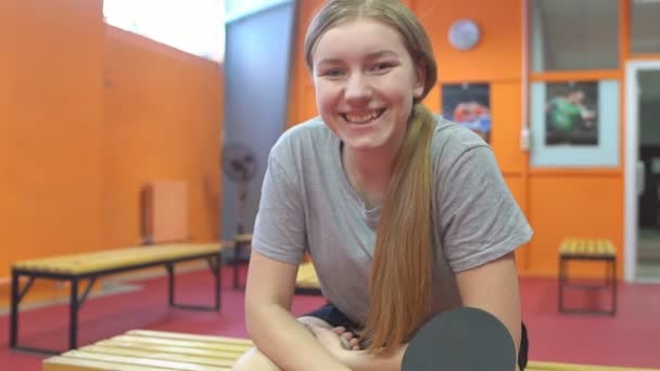 Porträtt av en leende kvinnlig bordtennisspelare med pingisracket sittande på en bänk — Stockvideo