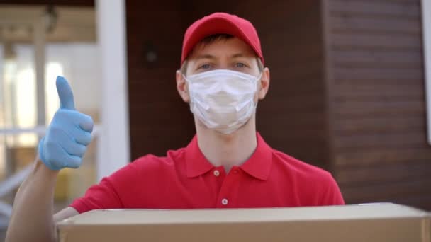Портрет рятувальника в масці безпеки, що тримає коробку з великими пальцями вгору. Служба доставки в карантинній коронавірусній ковірусі-19 . — стокове відео