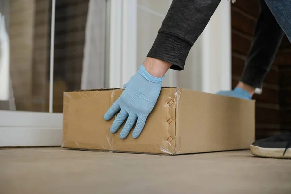 Доставщик в перчатках доставляет посылку к двери клиента. Крупный план бесконтактных поставок во время пандемии коронавируса. — стоковое фото