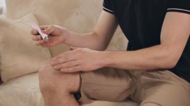 Adam hasta dizine medikal ağrı kesici merhem sürüyor. Diz atardamarı ağrıyormuş.