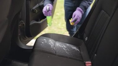 Eldivenli adam araba koltuklarındaki kiri temizlemek için köpük sabun spreyi kullanıyor.