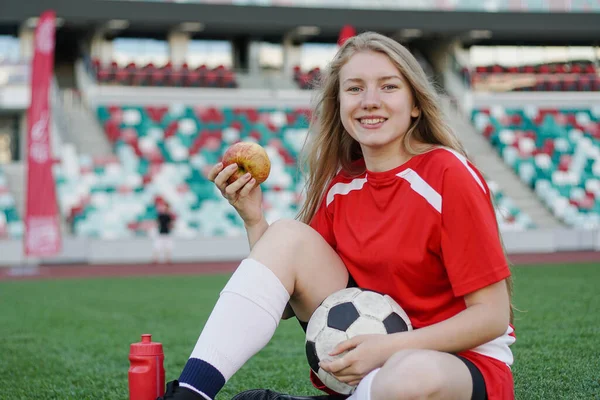 Portrét mladé fotbalistky sedící na fotbalovém hřišti s jablkem po tréninku — Stock fotografie