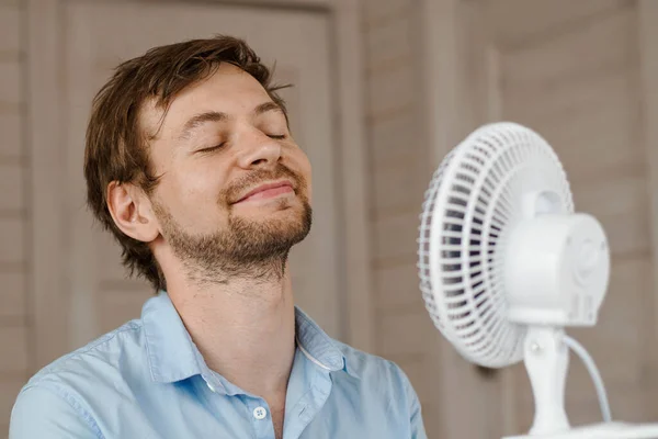 Hombre sudoroso disfrutando del flujo de aire del ventilador en la oficina. Empresario refrescante en frente de ventilador eléctrico de aire. —  Fotos de Stock