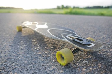 Gün batımında asfalt üzerinde sarı tekerlekleri olan uzun tahta.