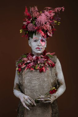 Kil bulaşmış bir kız. Modelde çiçeklerden yapılmış bir başlık var..