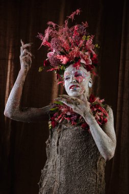 Kil bulaşmış bir kız. Modelde çiçeklerden yapılmış bir başlık var..