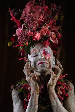 Kil bulaşmış bir kız. Modelde çiçeklerden yapılmış bir başlık var..