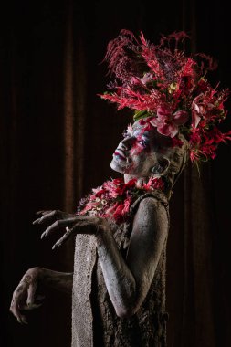 Kil bulaşmış bir kız. Modelde çiçeklerden yapılmış bir başlık var..