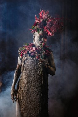 Kil bulaşmış bir kız. Modelde çiçeklerden yapılmış bir başlık var..