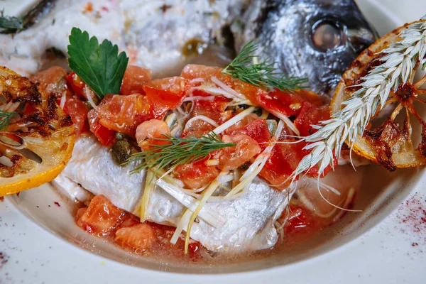 Boiled fish with sauce and fried tomatoes.