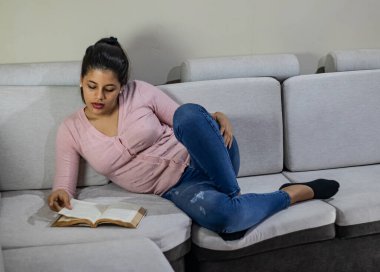 Evdeki kanepede kitap okuyan genç bir kadın.