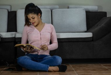 Oturma odasında kitap okuyan gülümseyen genç bir kadın.