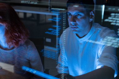 Profesyonel Bilişim Teknik Destek Uzmanı veya Yazılım Geliştiricisi bilgisayarların kontrol odasındaki kodu işaret edip analiz ediyor.