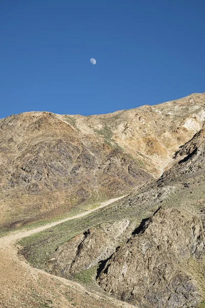 Moon rising over dirt mountain road — Stock Photo, Image