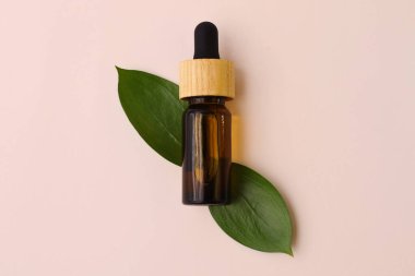 Kahverengi şeffaf bardaktan bir şişe şeffaf doğal yağ. Altında yeşil yapraklar. Düz konsept..