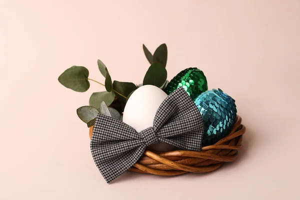 Natural egg in the bow tie in the rattan nest.Fresh eucalyptus branch on the background.Pastel color,copy space for text.Easter concept. — Stock Photo, Image