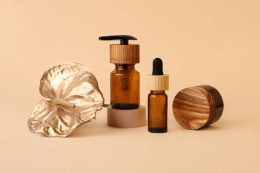 Tahta kapaklı çeşitli kozmetik kapları, nötr bej arka plan. Cam şişesi geometrik podyumda, yanında altın flamingo çiçeği duruyor. Sıfır atık, organik konsept. Modern minimalizm..