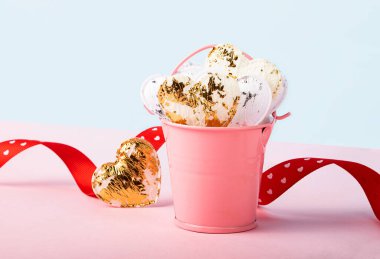 Beyaz kalplerle dolu küçük dekoratif pembe kova. Arka planda güzel kurdele. Moda eşölçülü pembe ve mavi arka plan. Sevgililer Günü kavramı..