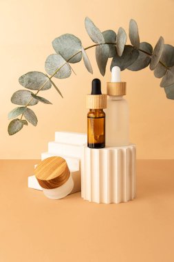 Geometrik podyumlardan ve cam kozmetik kaplarından gelen kompozisyon. Kemer gibi yukarıdan taze okaliptüs dalı. Isometric pastel arka plan. Kozmetik veya ürünleri göstermek için iyi bir model..