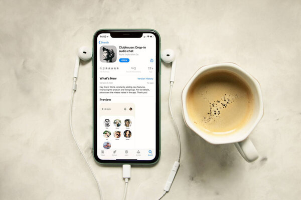 iPhone with clubhouse application on the phone screen,headphones next to it. New social network by Apple.Audio chat,concept of the morning routine.