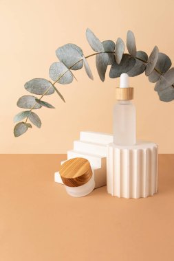 Geometrik podyumlardan ve cam kozmetik kaplarından gelen kompozisyon. Kemer gibi yukarıdan taze okaliptüs dalı. Isometric pastel arka plan. Kozmetik veya ürünleri göstermek için iyi bir model..