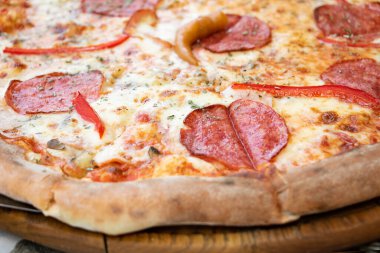 Taze pizzanın yakından çekilmiş fotoğrafı, dilimlere bölünmüş. Sosis, domates, peynir ve et parçalarıyla..