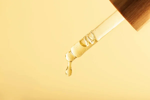 Petrol damlatan pipetin yakın plan fotoğrafı. Sıfır atık ahşap kaplama, sıcak sarı arka plan. Kozmetik modelleme konsepti..