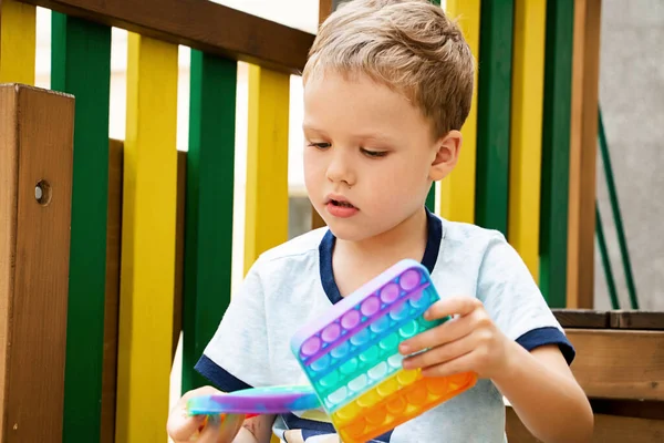 Kind spielt mit zwei neuen Silikon-Spielzeug Pop es auf dem playground.New sensorische Antistress-Spielzeug für Kinder und Erwachsene. Trendy Regenbogen-Färbung. — Stockfoto