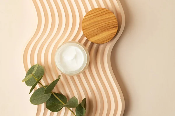 Open skin care packaging with white cream inside.Wooden cover near it. Box lying on the wavy podium.Pastel colors,good as mockup.