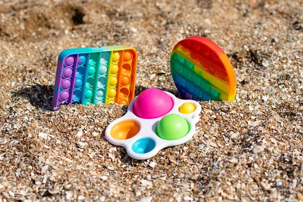 Conjunto de multicolorido pop-lo e covinha simples ficar na areia na praia, conceito criativo.Brinquedo anti-stress para crianças e adultos.Coloração arco-íris. — Fotografia de Stock