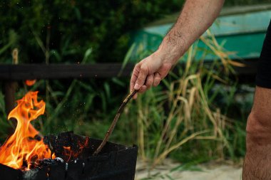 Bir adam elinde bir sopayla doğasında ateş yakar. Açık hava pikniği kavramı..