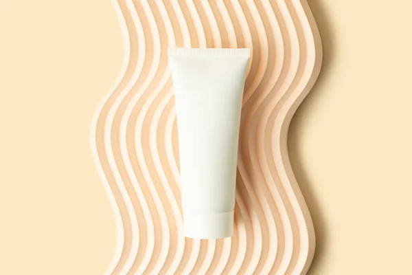 Blank white cosmetics tube on the beige background.Wavy podium under it.Good as cosmetic mockup,pastel banner with copy space.