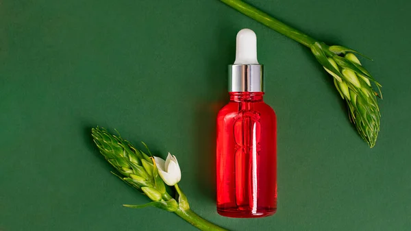 Red cosmetics bottle on the green background.Foliage with white flowers around,looks like frame.Cosmetic mockup with copy space,large banner.