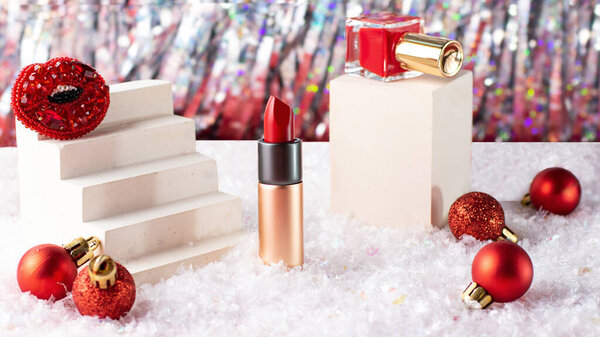 Composition from new year cosmetic-red nail polish bottle on the podium and lipstick.Bright background and snow below.Festive cosmetic concept.