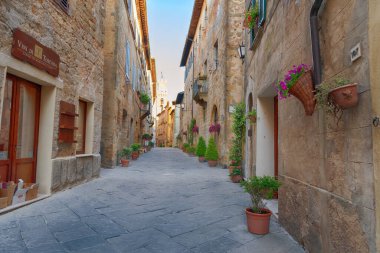 PIENZA, İtalya - 26 Mayıs 2017: Küçük sihirli ve eski Pienza köyü Val D 'Orcia Tuscany, İtalya' da güneş ışığı ve çiçeklerle dolu güzel dar bir cadde.
