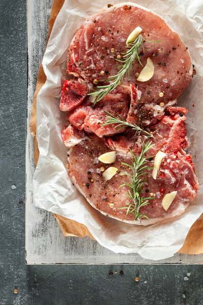 Two raw pork steaks grey stone background with rosemary and spices. Top view, copy space