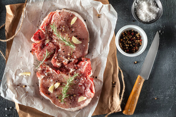 Two raw pork steaks grey stone background with rosemary and spices. Top view, copy space