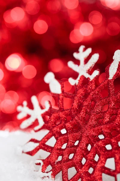Rode sneeuwvlok in sneeuw tegen rode vakantie lichten. — Stockfoto